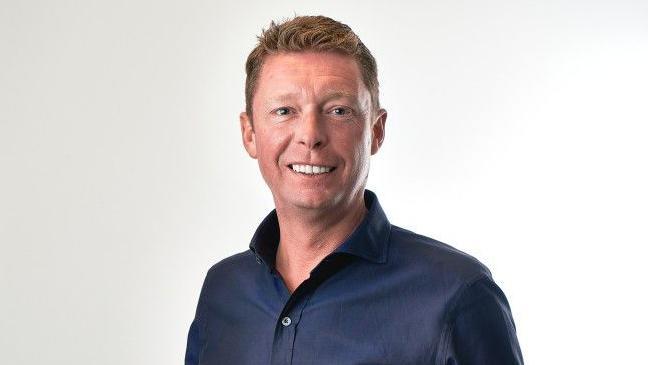 John Roberts, chief executive of AO, wearing a dark blue shirt and smiling directly at the camera