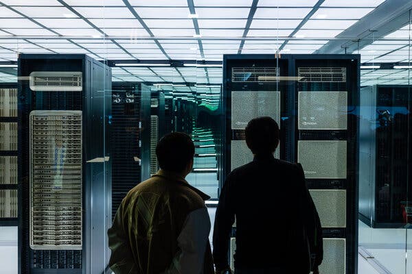 Two people look at rows of computers in a data center.