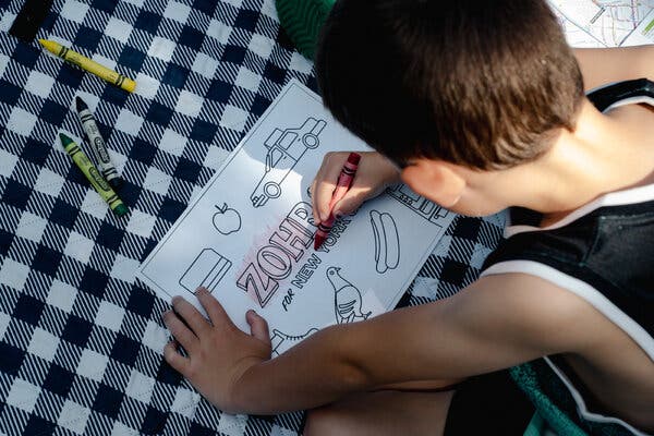 A boy uses crayons to color a Zohran for New York sheet of paper.