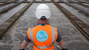 A Thames Water employee in a hard hat and orange vest looks at sewage water in aeration lanes.