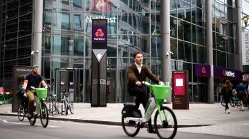 Two cyclists ride e-bikes past the NatWest bank headquarters in London.
