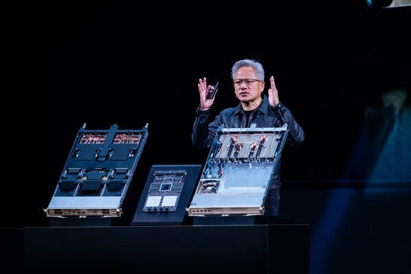 Jensen Huang gesturing as he stands behind computer chips.