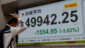 A man combs his hair while watching a stock quotation board showing the Nikkei share average in Tokyo.