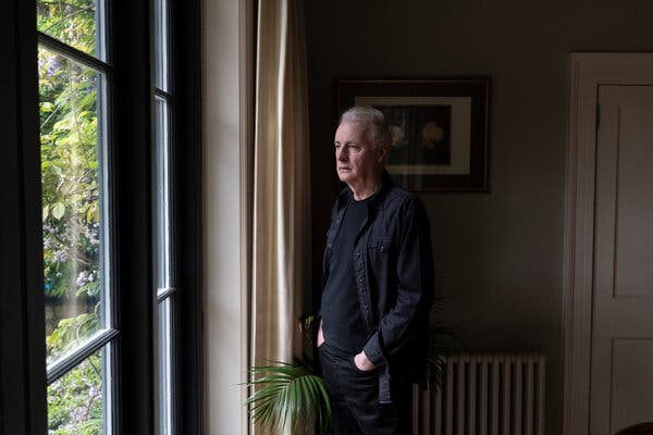 Dave Fanning, standing with his hands hin his pants pockets, looks out a window in his home.
