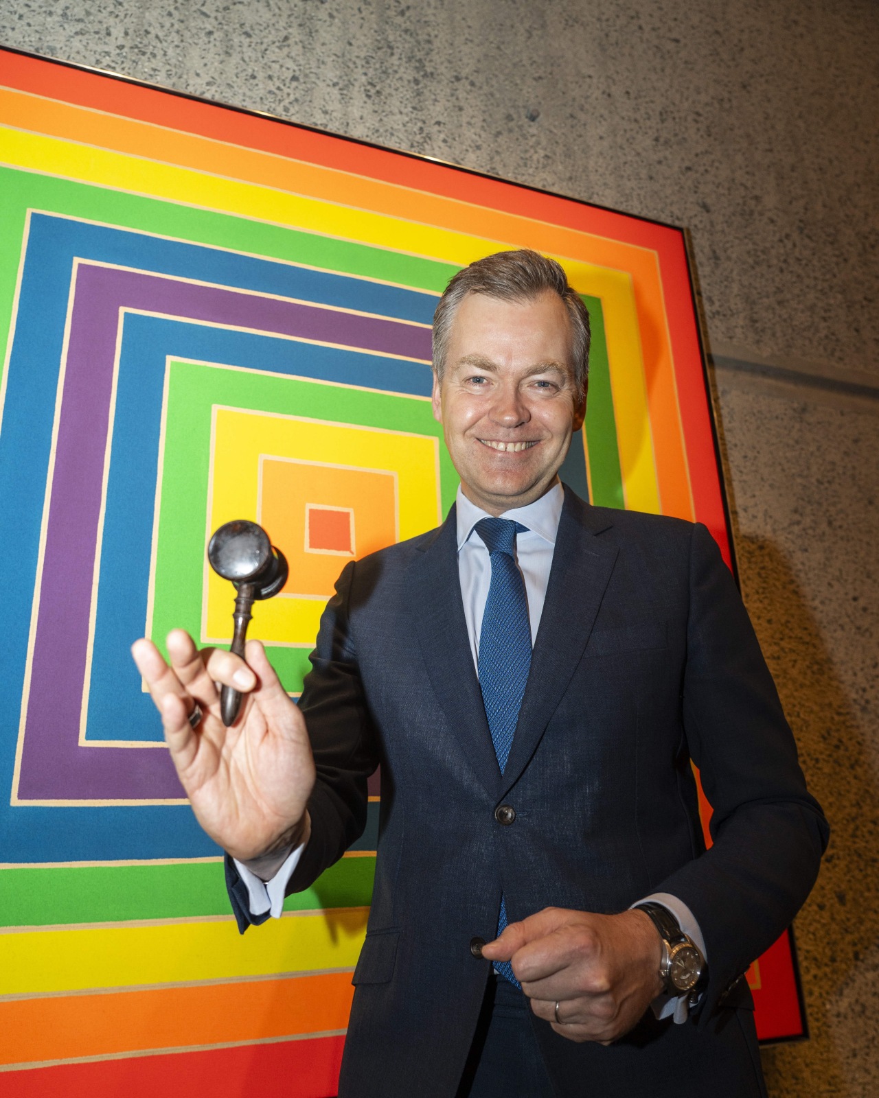 Oliver Barker, the principal auctioneer at Sotheby's, holding a gavel in front of a colorful, geometric artwork.