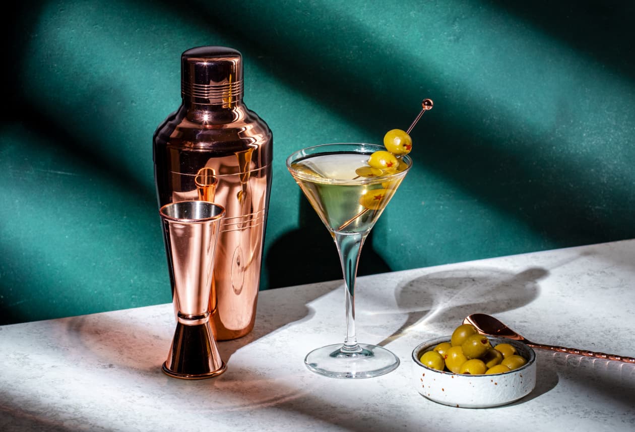 Martini glass with olives, cocktail shaker, jigger, and a bowl of olives.