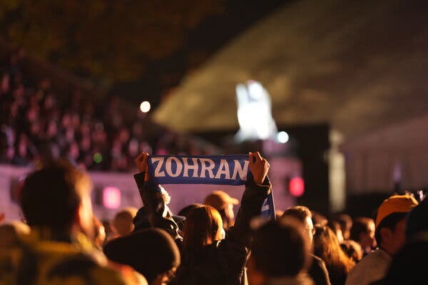 A supporter holds aloft part of a Zohran Mamdani banner, with only the first name visible, at Forest Hills Stadium.