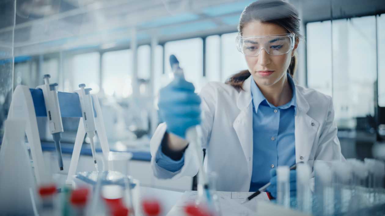 Female scientist in goggles using a micro pipette in a laboratory.