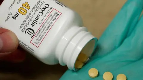 Reuters A hand holds a white bottle reading "OxyContin", pouring out small round pills.