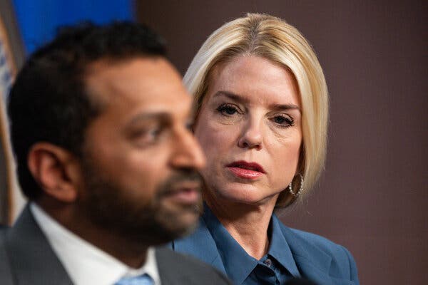 Attorney General Pam Bondi, wearing a blue top, looks at Kash Patel, the F.B.I. director, who is blurred in front of her.