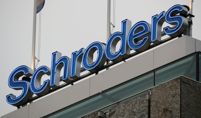 The illuminated blue "Schroders" logo on top of a building.