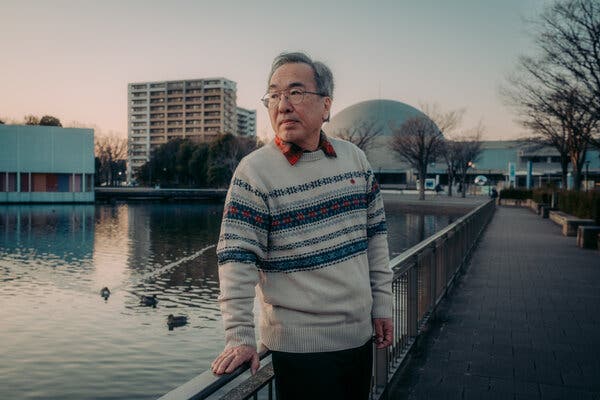 Hiroyuki Kubota standing at a railing overlooking a body of water, with some buildings in the background. 