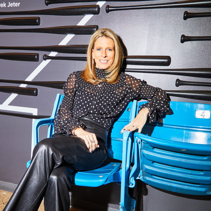Amy Howe, CEO of FanDuel, sitting in a blue stadium seat in front of a wall with baseball bats.
