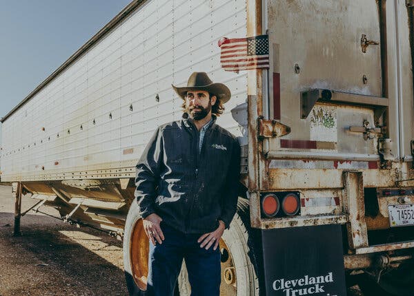 Mr. Westerfield, wearing a brown cowboy hat, blue jacket and jeans, leans against a tractor trailer.
