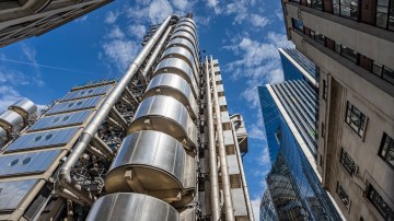 Looking up at the Lloyds of London Building in the heart of London's financial district under a blue sky.