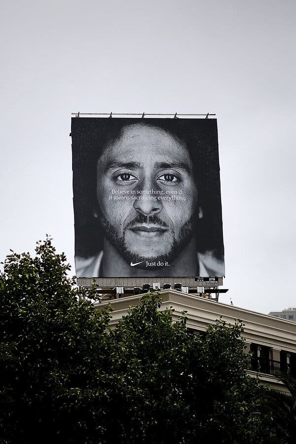 A large black-and-white billboard on top of a beige building says, “Believe in something, even if it means sacrificing everything,” over a photo of Colin Kaepernick.