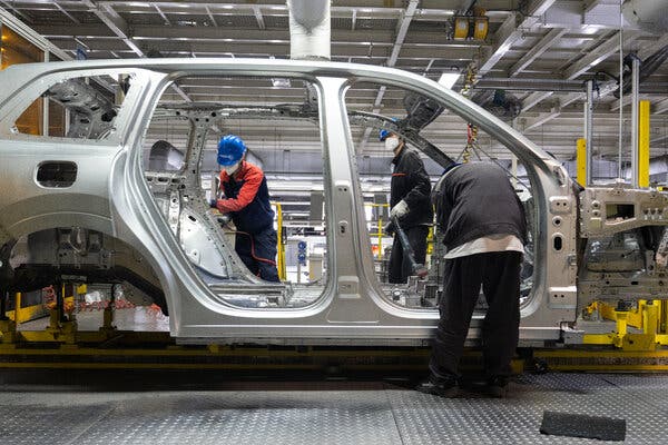 Three people on an auto assembly line work on the outer shell of a car’s body. 