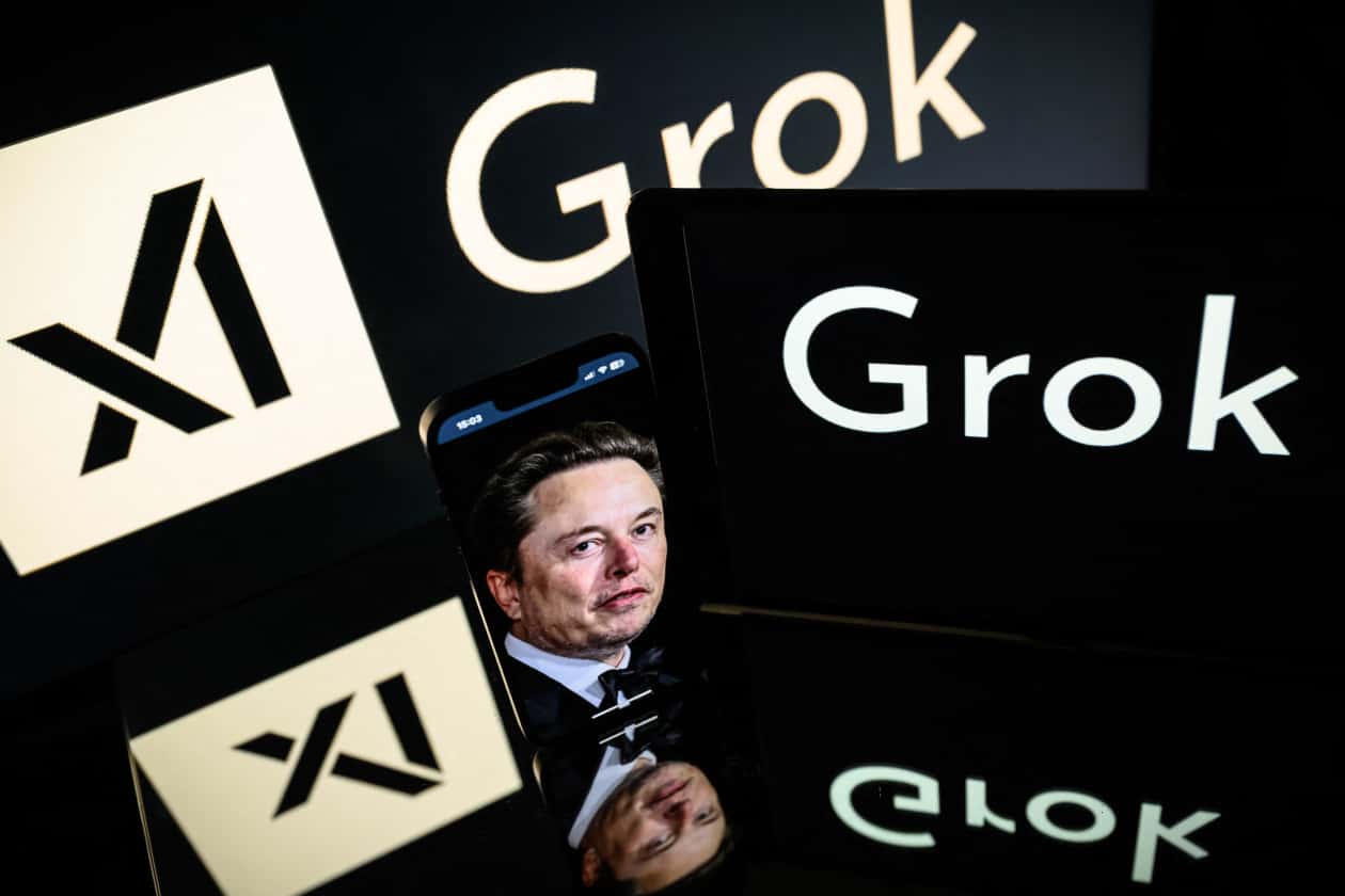 Screens displaying the Grok AI logo with Elon Musk's face on a phone in the foreground.