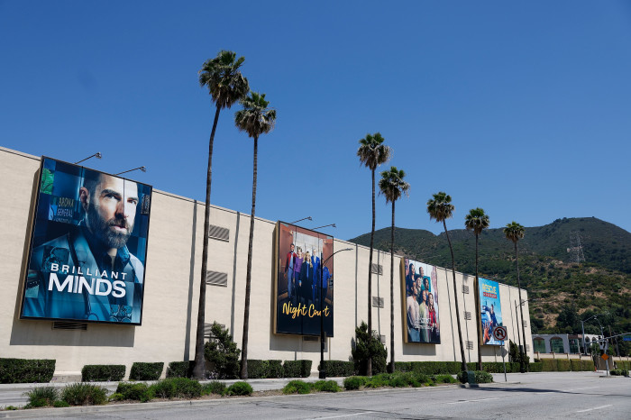 Warner Bros. studios in Burbank, California, with billboards for "Brilliant Minds," "Night Court," and other shows.