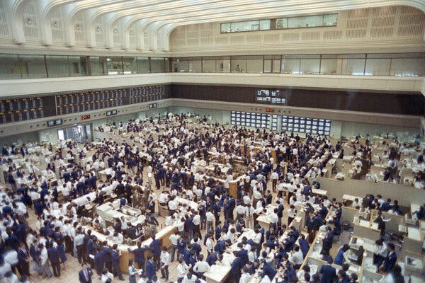 An overhead view of a large, crowded trading floor, with people wearing either blue jackets or white shirts. 