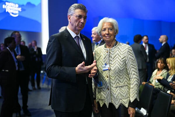 Christine Lagarde, smiling, and Andrej Plenkovic, gesturing, stand in a blue room. A 'World Economic Forum' sign is visible in the background.