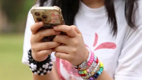 Reuters Teen girl wearing a clutter of colourful bracelets on her wrist as she types on her smartphone.