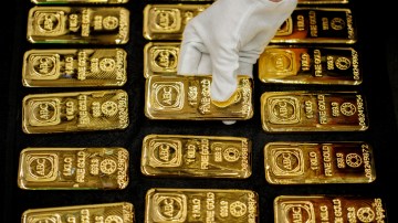 A gloved hand places a one-kilogram ABC gold bar among several others.