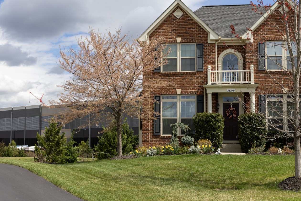 A brick house in the foreground with a large data center visible behind it, showcasing the impact of development in Loudoun County.