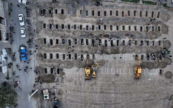 An aerial photo shows rows of small graves being dug by yellow excavators and workmen inside the graves at a cemetery.