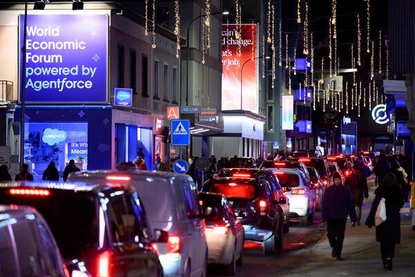 A street at night with vehicles and pedestrians. Buildings are lit by blue light, and string lights hang overhead.