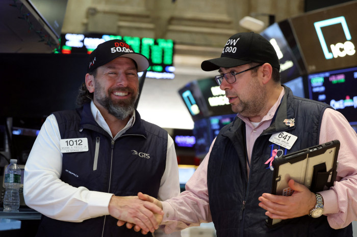 Traders shaking hands, wearing caps that say "DOW 50,000" on the floor of the New York Stock Exchange.