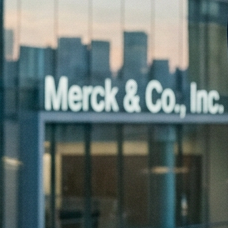 Two businesswomen shaking hands over a scale model of Merck and Bio-Techne office buildings