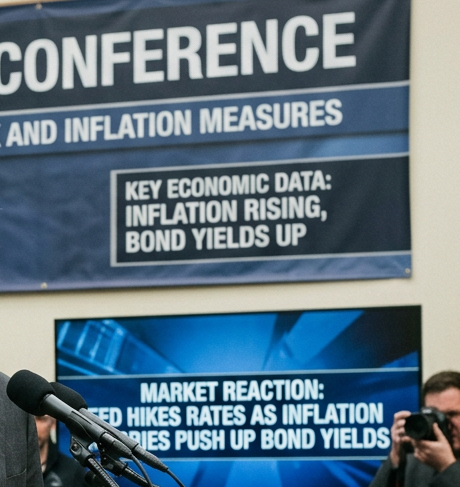 Speaker at podium beneath PRESS CONFERENCE banner about economic outlook and inflation measures